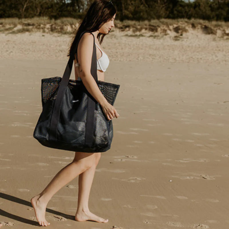 Walking on sand carrying shoulder Sande Kids beach bag in navy.