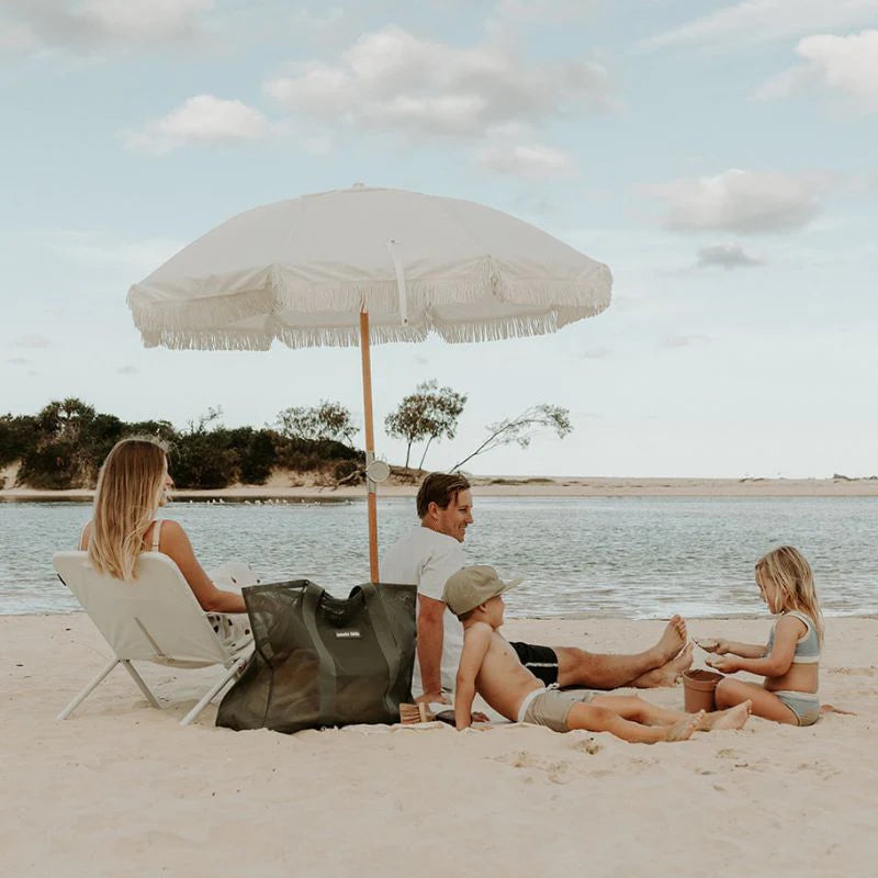 Family at lake on sand under umbrella with large beach bag.