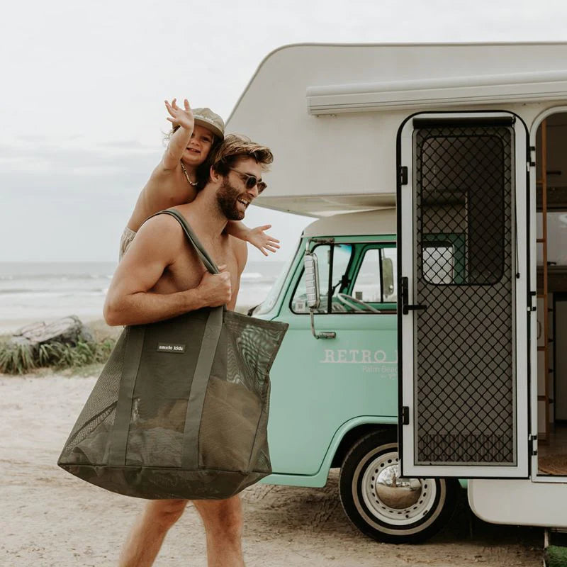 Dad next to caravan with toddler and beach bag on shoulder.