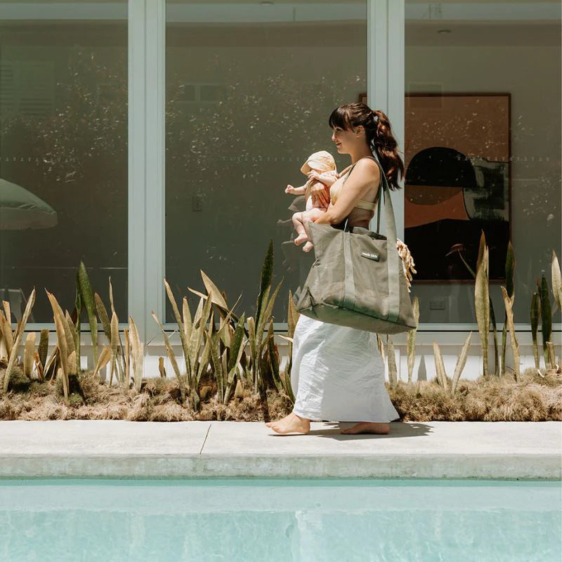 Sande Kids Beach Bag in Olive Green being carried by Mum with baby in arms near a backyard pool.