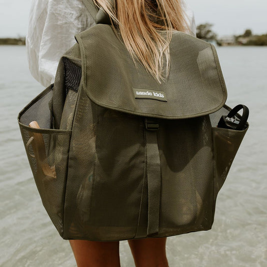 Person wearing a green backpack with 'sande kids' branding by a body of water.